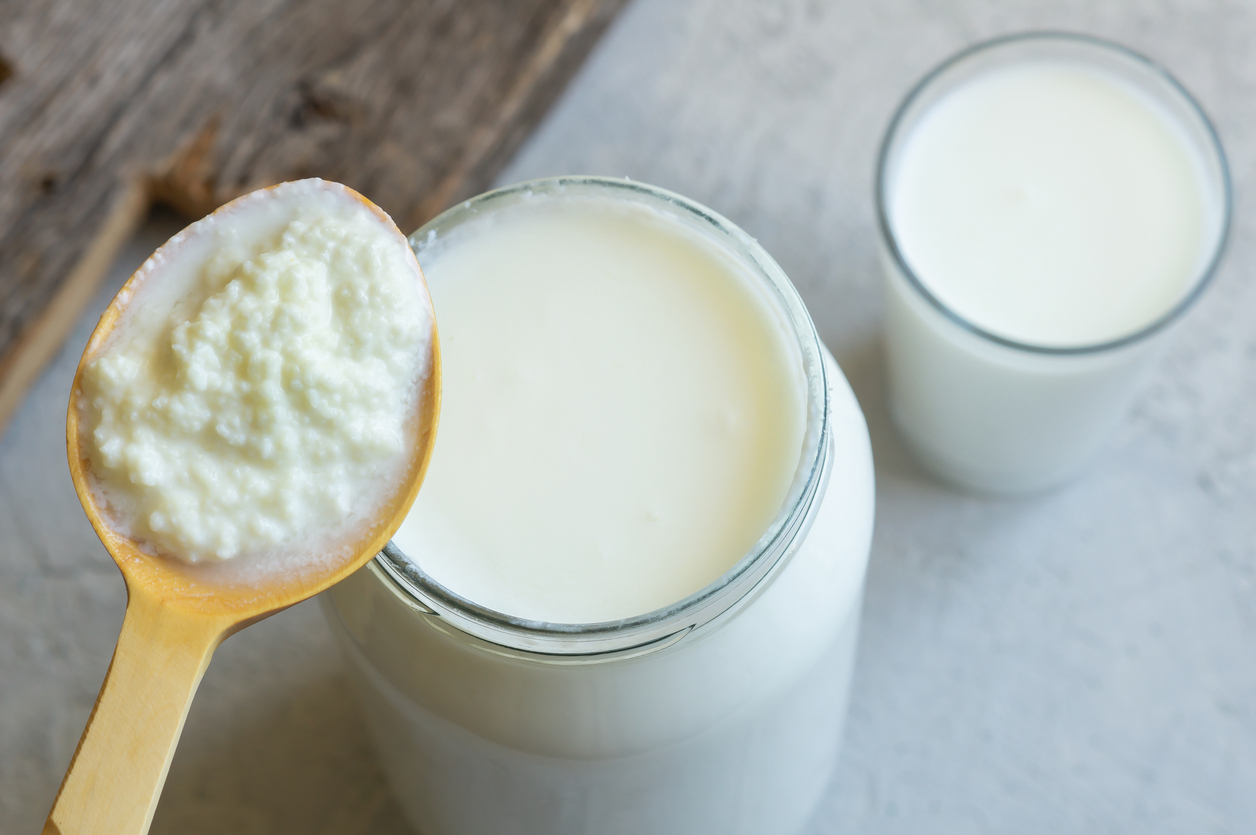 Kefir grains in wooden spoon with glass of kefir drink, healthy fermented probiotic cold dairy drink