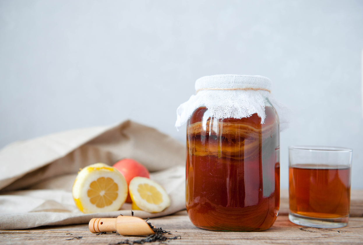 Homemade fermented kombucha tea in a glass jar and in a glass cup on a wooden and gray background.